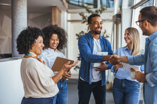 A diverse group of professionals smiling and shaking hands in a modern office environment. The image conveys teamwork, collaboration, and positive business relationships.